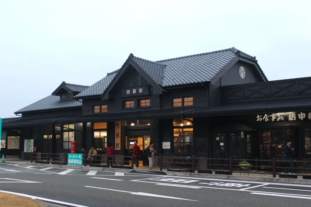Dark-timbered station building and forecourt at Aso Station, Kumamoto