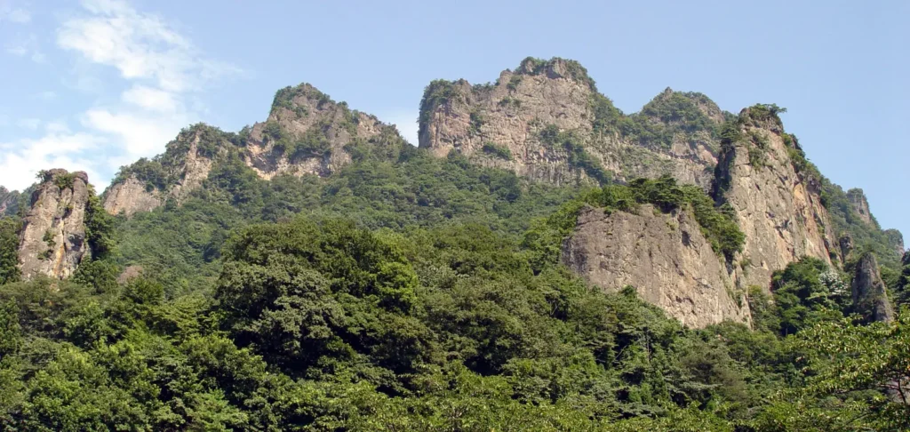 Jagged bare rock pinnacles of Mount Myogi above forested slopes under a blue sky, Gunma