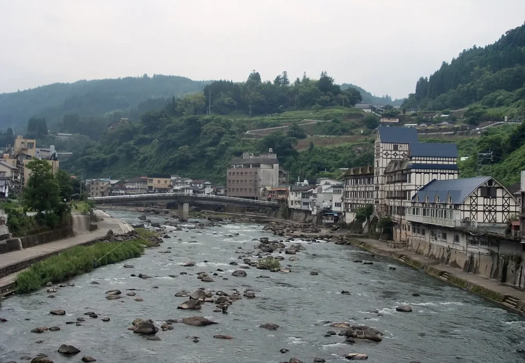 Rocky river running between hot spring inns and forested hills at Amagase Onsen, Hita, Oita