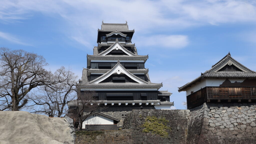 Reconstructed main keep of Kumamoto Castle rising above stone walls under a blue sky