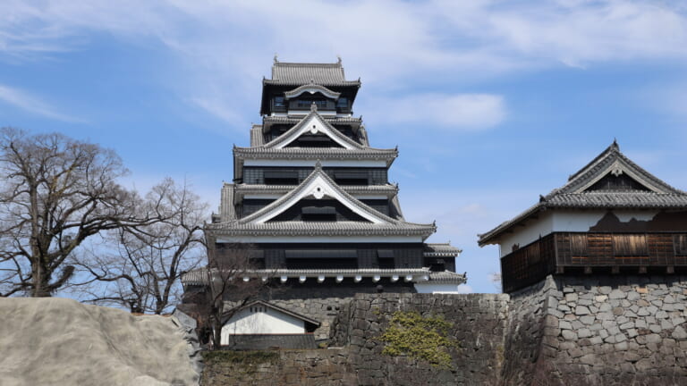 Reconstructed main keep of Kumamoto Castle rising above stone walls under a blue sky