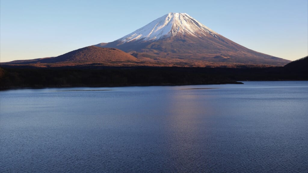 Snow-capped Mount Fuji reflected in the still water of Lake Motosu