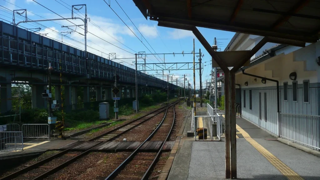 The single-track platform of Toyosato Station on the Ohmi Railway, with a station building on the right and an elevated railway line on the left