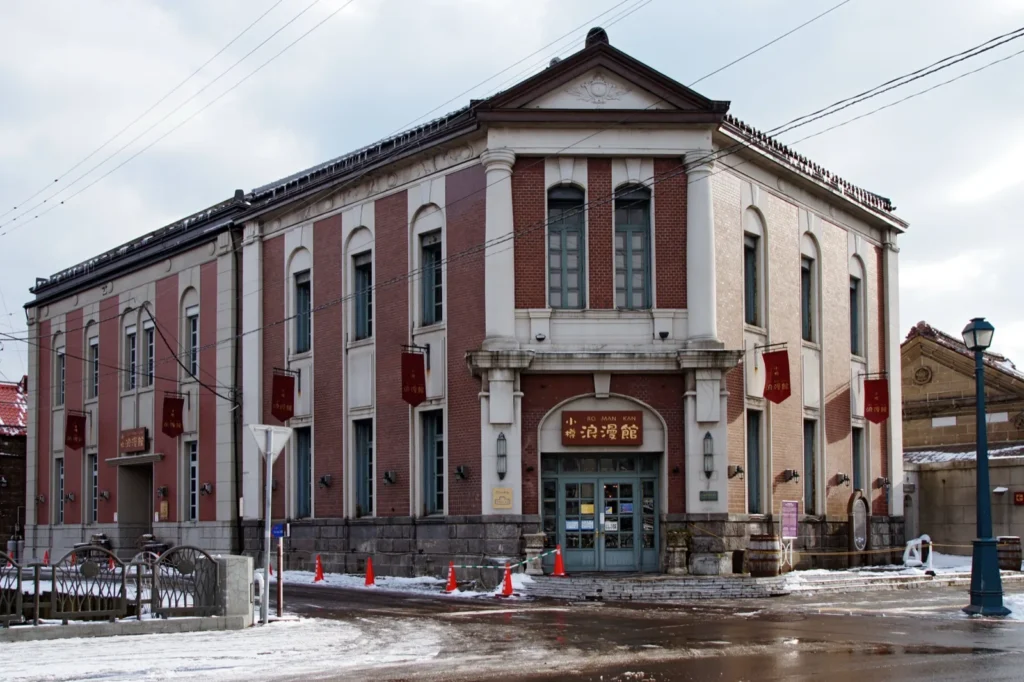 The red-brick and white-stone front of Otaru Romankan, the former Hyakujusan Bank Otaru branch, on a snowy street
