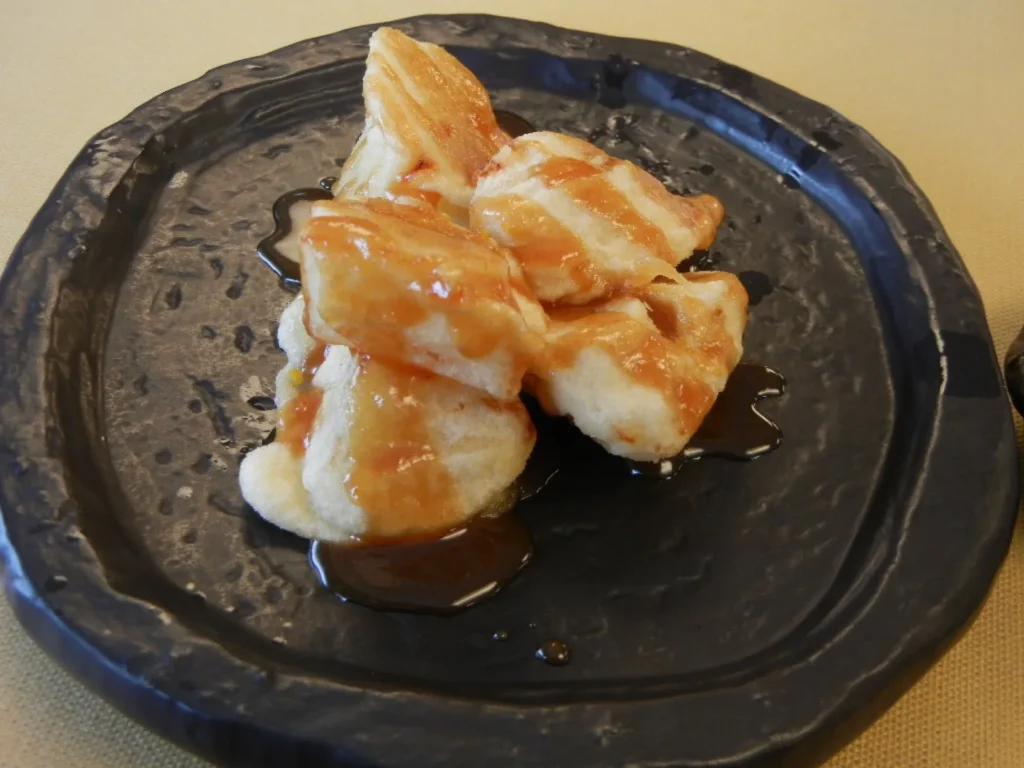 Battered potato pieces under a sweet miso sauce on a dark plate