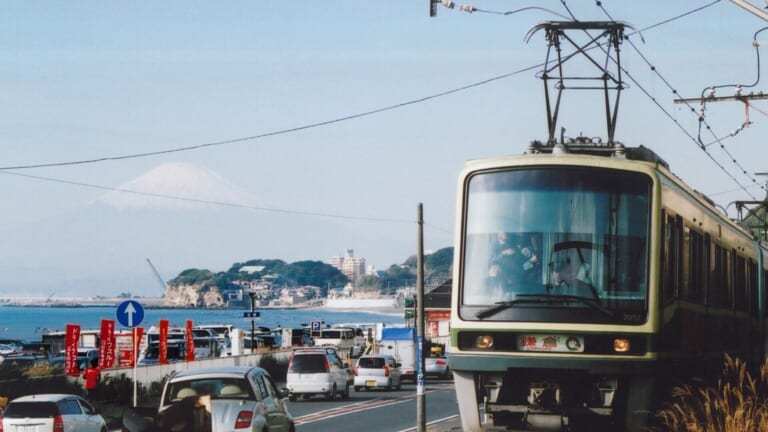 A green and cream Enoden train running beside the Shonan coast with Mount Fuji behind it