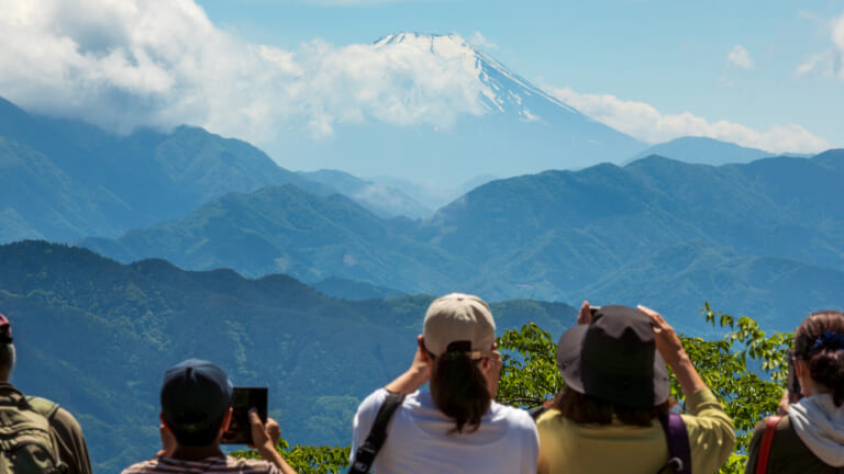 Walkers at the summit of Mount Takao photographing Mount Fuji rising above ridges of hills