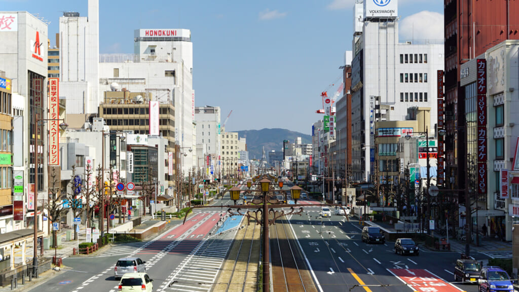 The wide Ekimae-Odori boulevard outside Toyohashi Station with tram tracks down the middle and hills on the horizon