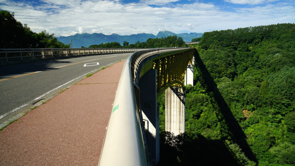 The Yatsugatake Kogen Ohashi bridge curving across a wooded gorge with the Southern Alps on the horizon