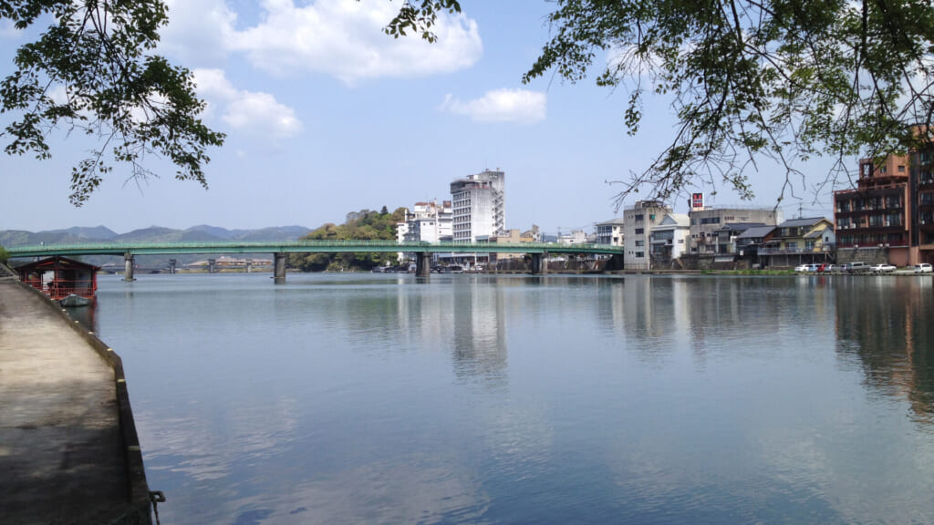 The Mikuma River at Hita with the green truss bridge, riverside hotels and the wooded hill of Kameyama Park
