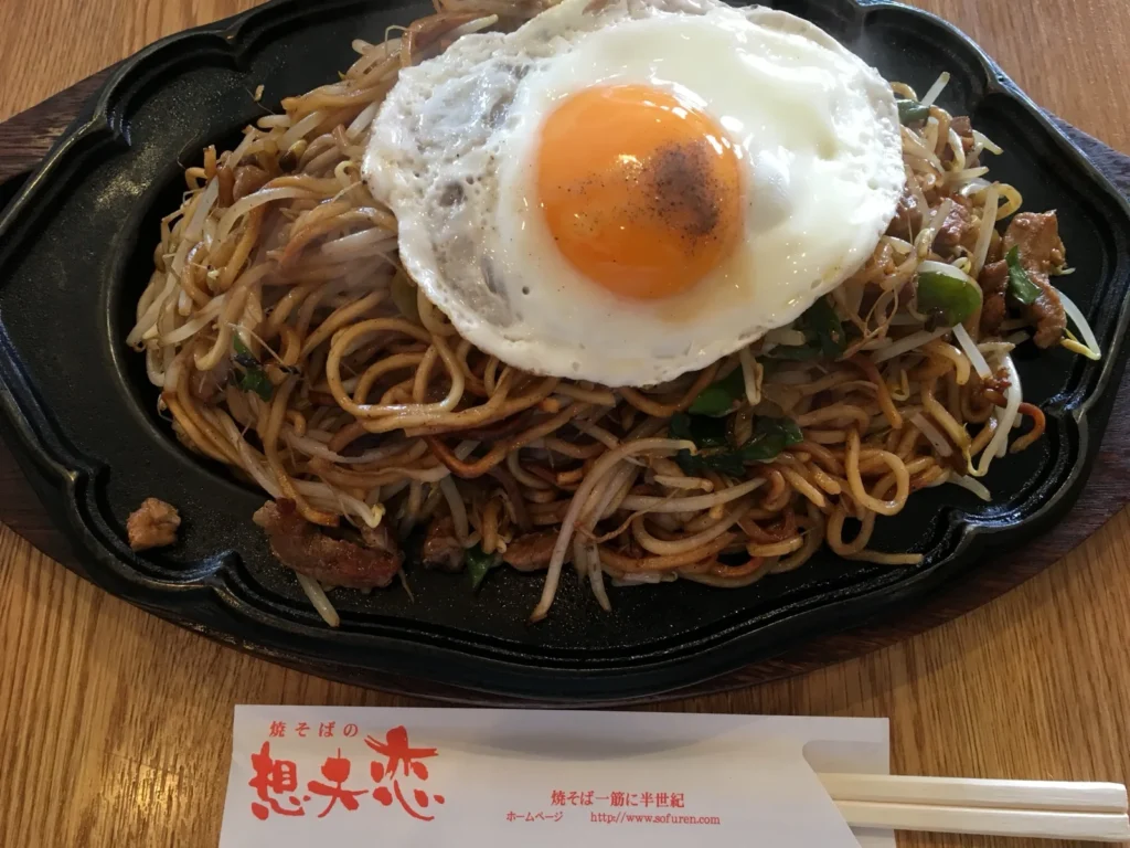 A plate of Hita yakisoba on a hot iron plate, the noodles crisped at the edges, with bean sprouts and a fried egg on top