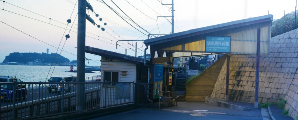 Kamakurakokomae Station at dusk with the level crossing and Enoshima across the bay