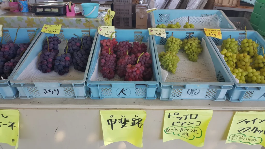 Trays of different grape varieties on sale at a roadside stall in Katsunuma with handwritten variety labels