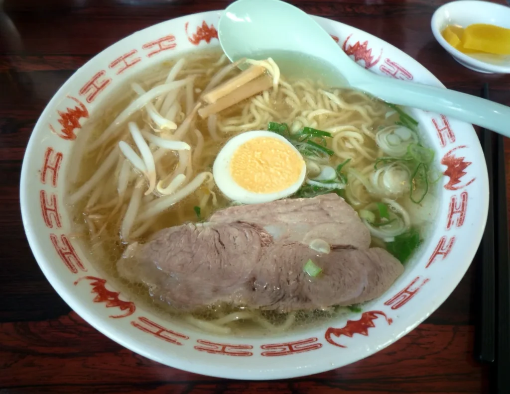 A bowl of Tottori beef-bone ramen in a clear broth with sliced pork, bean sprouts, menma, spring onion and half a boiled egg
