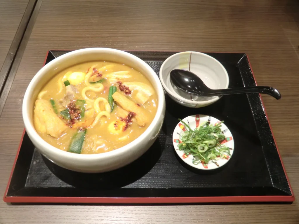A bowl of Toyohashi curry udon on a tray, with a spoon and a side dish of pickles