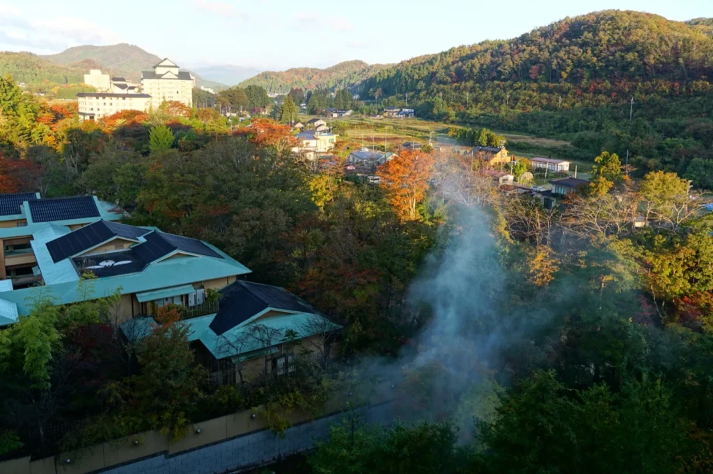Hot-spring hotels among autumn trees in the Akiu valley, with steam rising and hills behind