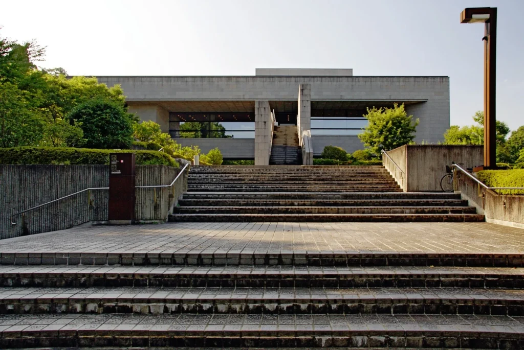 Wide stone steps leading up to the concrete front of Sendai City Museum among trees