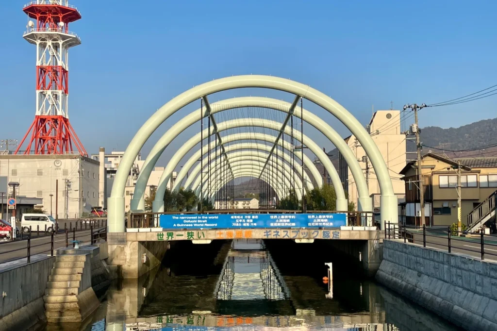 The Dofuchi Strait, a narrow channel between concrete banks, passing under a row of white arches
