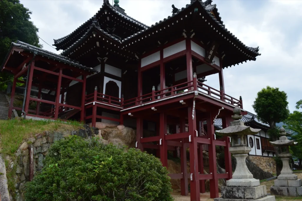 The vermilion Fumeikaku hall of Saihoji temple standing on wooden stilts above a stone wall, with stone lanterns in front