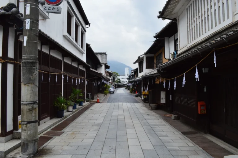 A quiet paved street in Takehara's old town, lined with white-walled merchant houses with dark wooden lattices and paper streamers