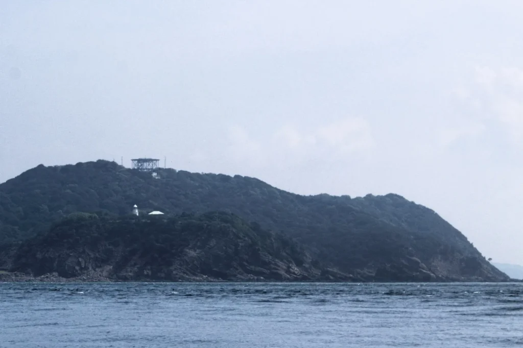 The wooded western end of Okinoshima seen across the sea, with the small white Tomogashima Lighthouse on the slope