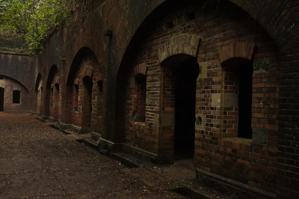 A row of arched brick rooms with dark doorways at the Battery No. 3 ruins on Tomogashima, with fallen leaves on the ground