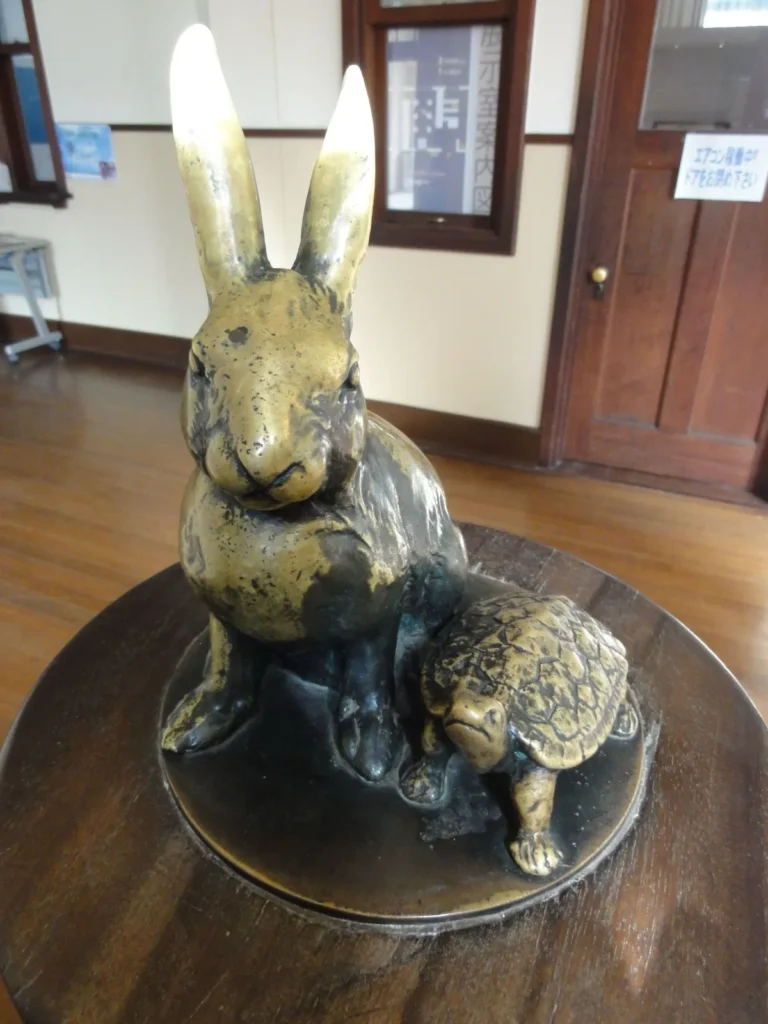 A small bronze rabbit and tortoise on top of a wooden newel post at the foot of a staircase in the old school