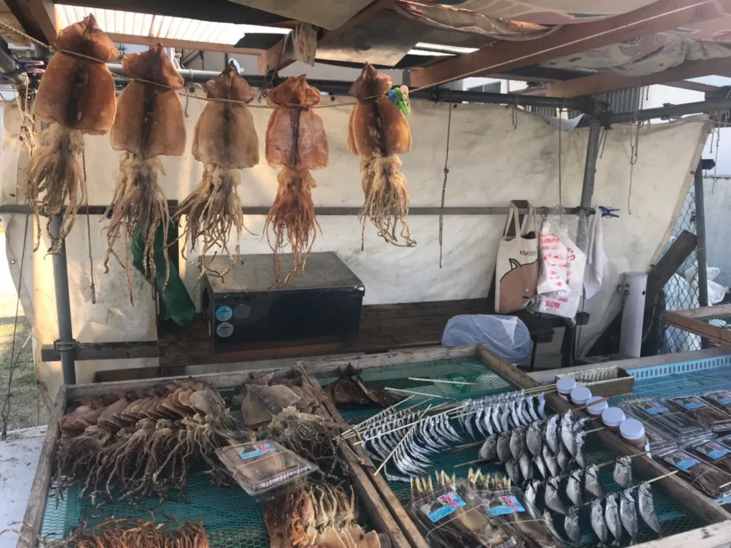 Dried squid hanging above a market stall in Yobuko, with trays of dried squid and fish below