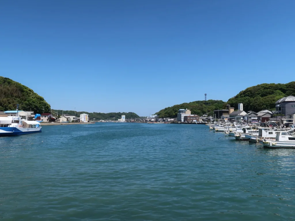 Fishing boats moored along the quays of Yobuko Port under a blue sky, with wooded hills on both sides