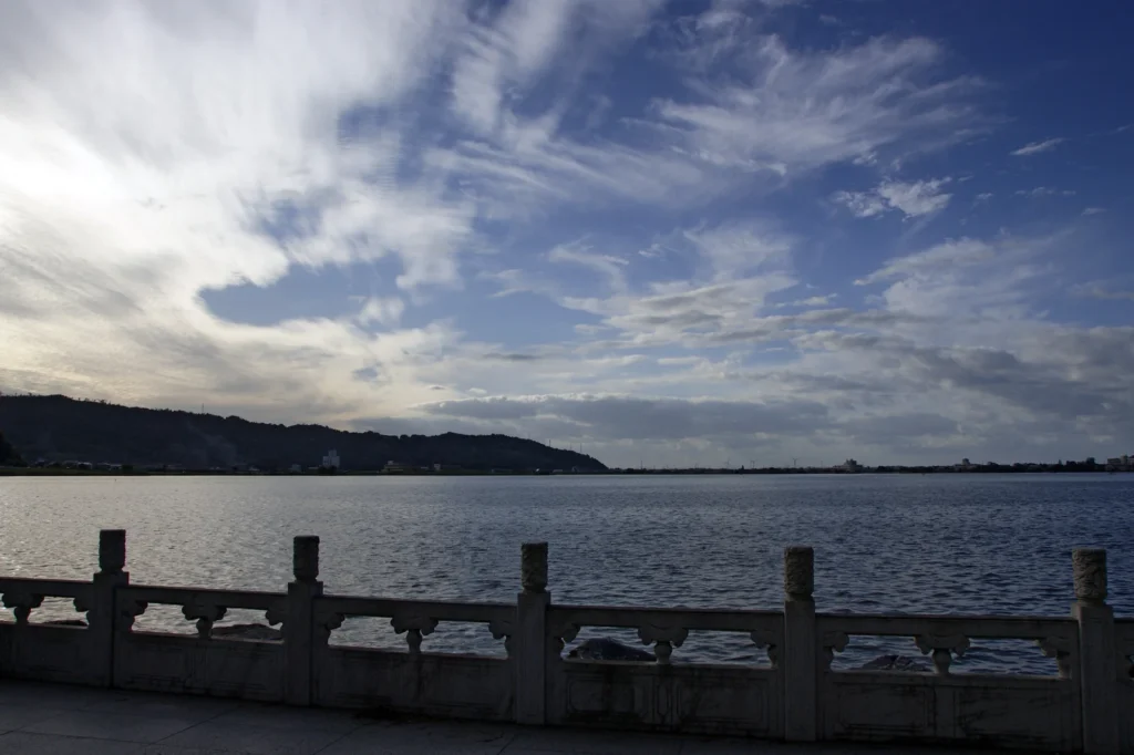 Stone balustrade beside Lake Togo with low hills and clouds across the water, Yurihama, Tottori